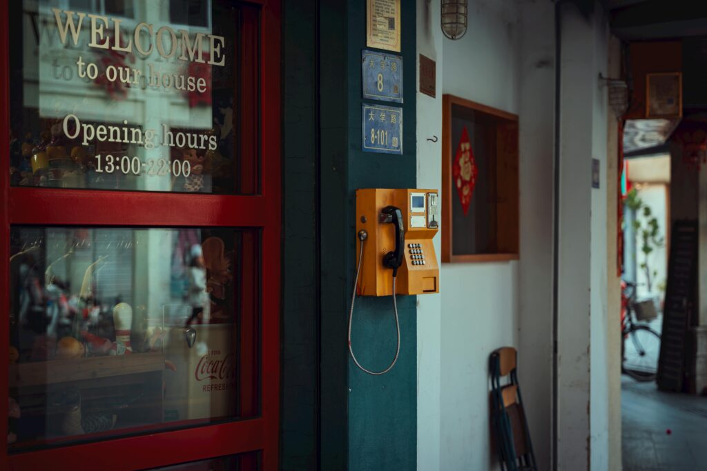Retro orange payphone on a blue wall with glass door reflection, capturing urban charm in Xiamen, China.