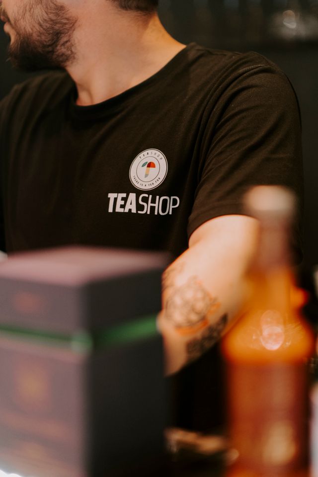Close-up of a barista in a black t-shirt with a tea shop logo, serving drinks.