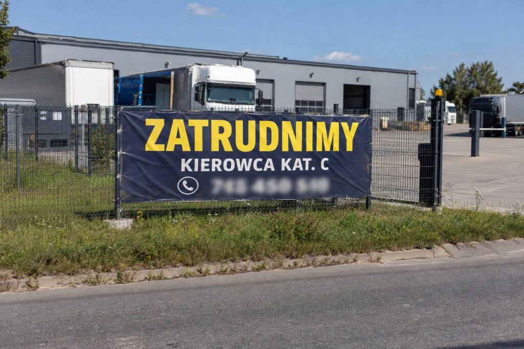 Granatowy baner rekrutacyjny ZATRUDNIMY KIEROWCA KAT. C na ogrodzeniu bazy transportowej